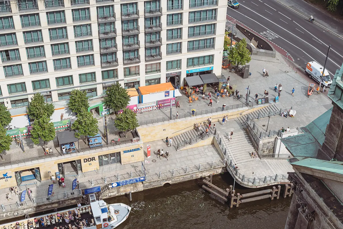 Aerial view of the Spree promenade below Berlin Cathedral, with the DDR Museum sign above the entrance and steps leading down from the street